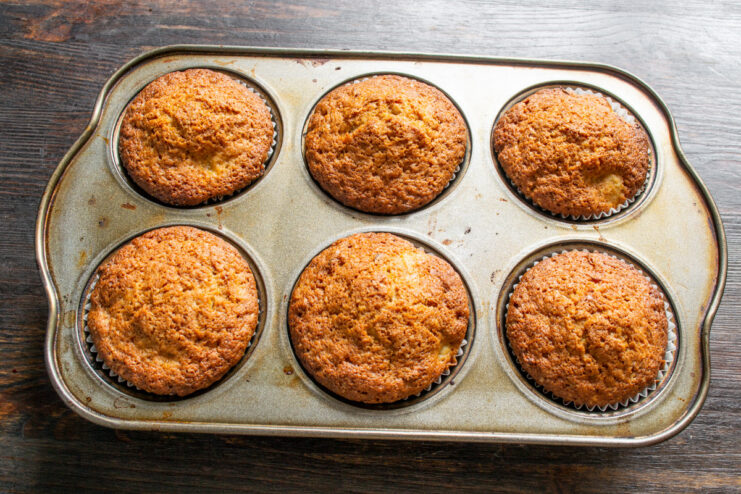 Step 8: Baking the muffins until golden brown and cooked through A muffin tin with orange and cinnamon muffins baking in the oven.
