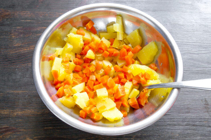 Adding Diced Carrots to the Potato Salad Diced boiled carrots being added to a bowl of diced potatoes for the salad.