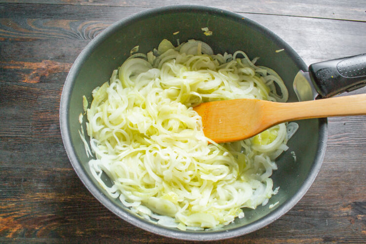 Sweating the Onions to Release Moisture Sliced onions cooking in a large skillet with butter, covered with a lid.