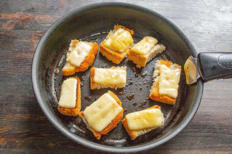 Making Crispy, Cheesy Croutons for the Soup Topping Slices of white bread being toasted in a pan, topped with cheese.