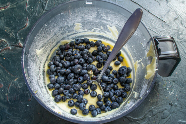 Gently folding in fresh blueberries for juicy bursts of flavor Fresh blueberries being added to the thick muffin batter in a bowl.