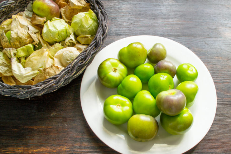 Step-by-step: How to properly wash physalis before pickling. Husked green and purple physalis berries being washed in a bowl of water.