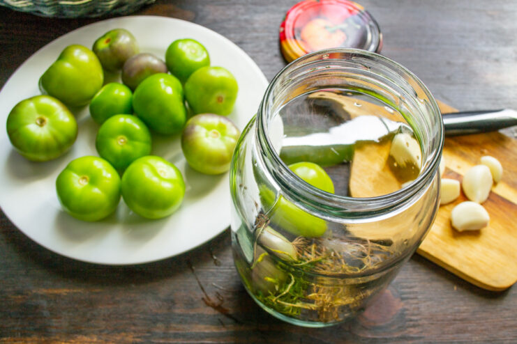 Layering physalis and garlic in a jar for the perfect flavor infusion. A hand placing whole garlic cloves into a glass jar layered with physalis.