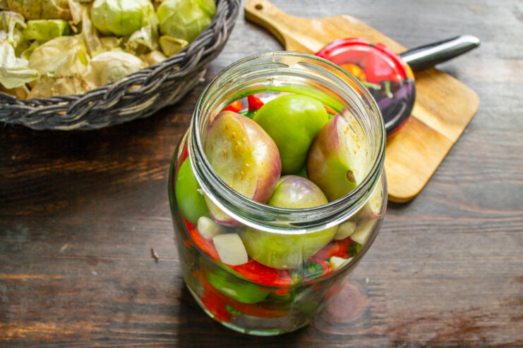 A perfectly packed jar of physalis, chili, and garlic ready for the brine. A glass jar filled to the brim with physalis, chili peppers, and garlic.