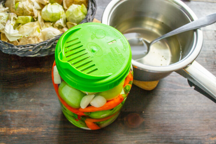 The double boiling water method for sterilizing vegetables in the jar. Pouring boiling water from a kettle into a jar of physalis and peppers.