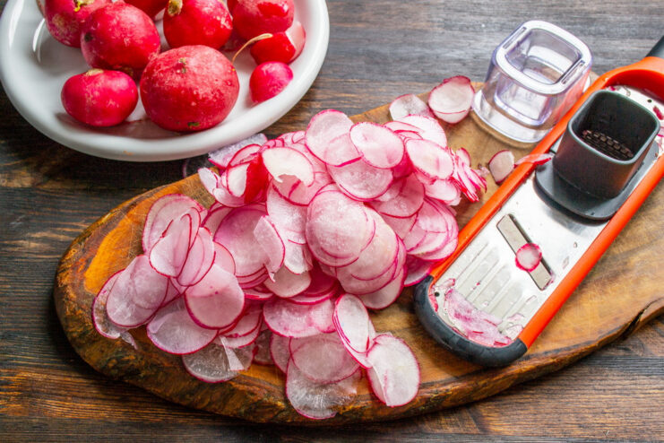 How to Perfectly Slice Radishes for Pickling A hand using a mandoline slicer to cut a red radish into paper-thin slices.