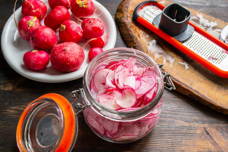 Packing Sliced Radishes into a Jar for Marinating Sliced red and white radishes being placed into a clear glass jar.