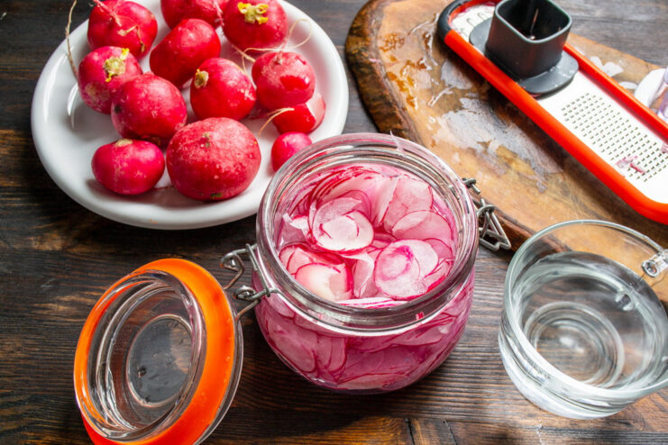 Measuring the Right Amount of Water for the Marinade A glass jar with sliced radishes being filled with cold water from a tap.