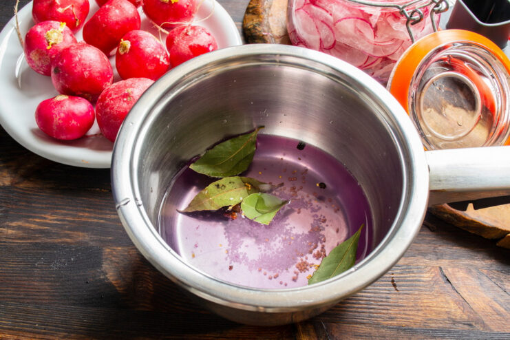 Preparing the Aromatic Marinade for Pickled Radishes A saucepan on a stove with a simmering marinade containing spices like bay leaves and peppercorns.