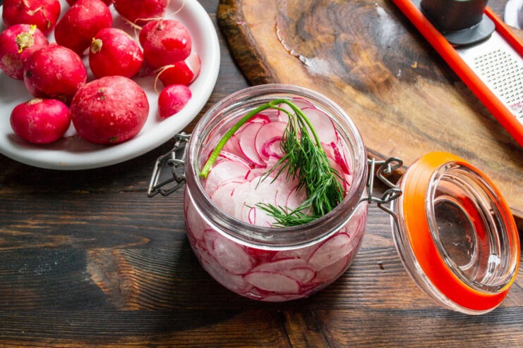 Adding Fresh Dill for Extra Flavor A sprig of fresh green dill being added to a jar of sliced radishes.