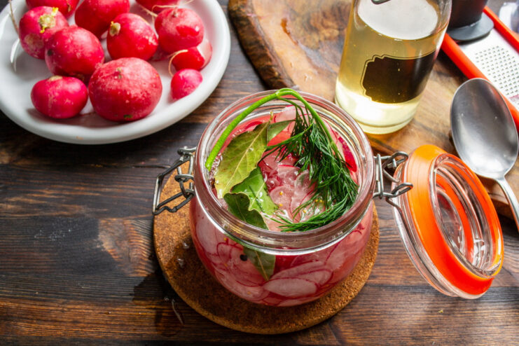Ensuring Radishes are Fully Submerged in Marinade A jar of sliced radishes completely covered with the pickling liquid and a sprig of dill.