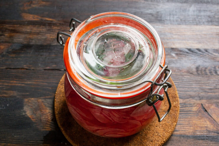 Properly Sealing the Jar for Marinating A hand tightly screwing the lid onto a glass jar of marinated radishes.