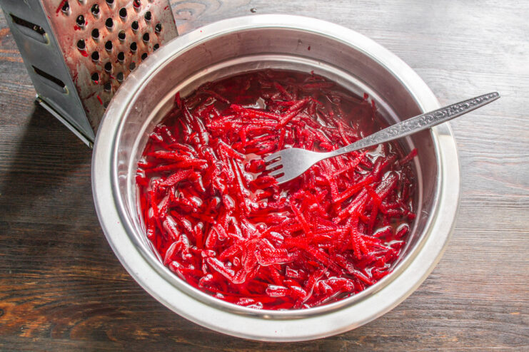 A useful tip: Rinsing the beets helps to remove excess juice and prevent staining. Grated beets in a bowl, being rinsed with water to reduce color bleeding.