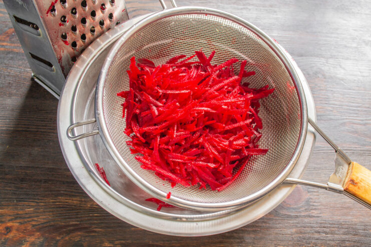 Make sure to drain the beets well to avoid a watery salad. Grated beets being drained in a white colander over a sink.