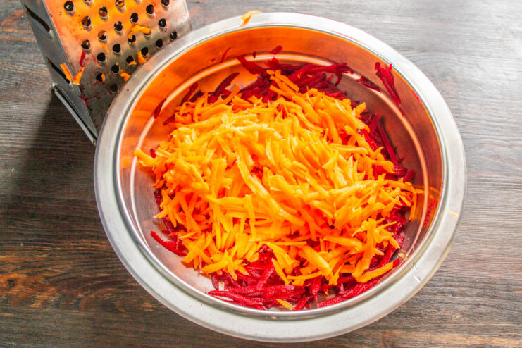 Step 2: Adding freshly grated carrots for sweetness and crunch. A hand grating a fresh carrot on a coarse grater into a bowl.