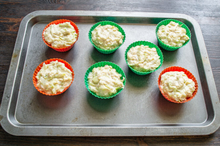 Filling Silicone Molds with Batter Spoonfuls of zucchini batter being placed into red silicone muffin cups.