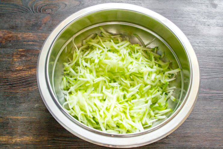 Grating Zucchini for the Casserole Batter Peeled zucchini being grated on a coarse box grater into a bowl.