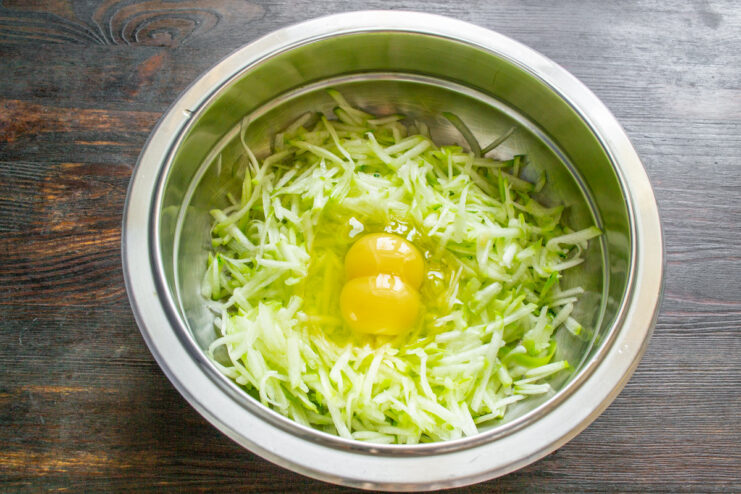 Adding Eggs to the Zucchini Mixture Two eggs cracked into a bowl with grated zucchini.