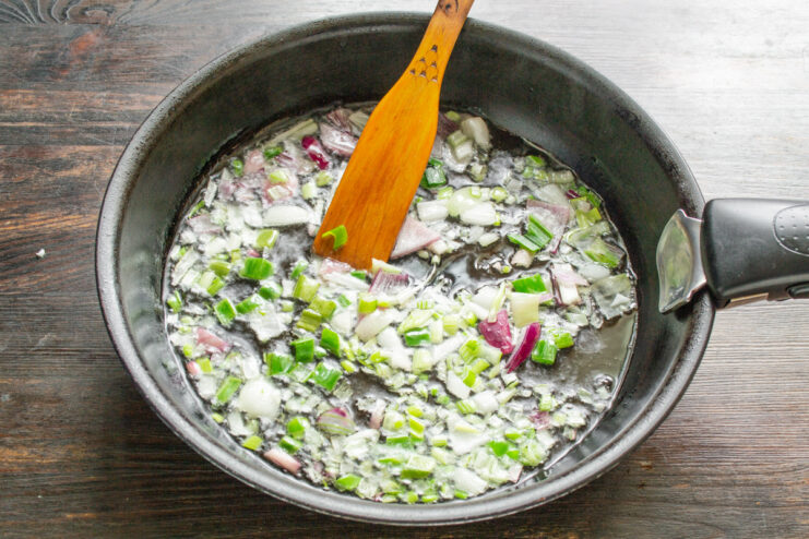 Finely chopping the white parts of green onions for frying. Close-up of finely chopped green onions on a cutting board.