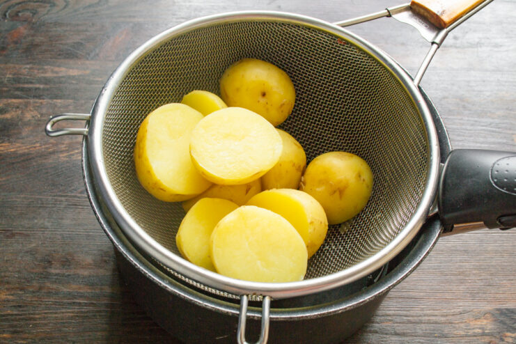 Draining the par-cooked potatoes to let them dry before frying. Par-cooked new potatoes being drained in a metal colander.