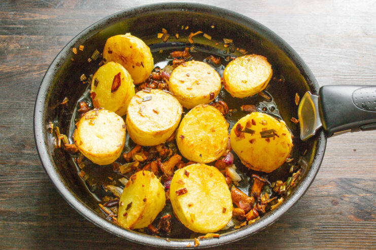 Flipping the potatoes to ensure they are golden brown on all sides. Golden-brown fried new potatoes being turned over in a skillet with a spatula.