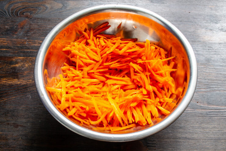 Grating Carrots for the Pizza Crust A close-up shot of carrots being grated on a coarse box grater into a bowl.