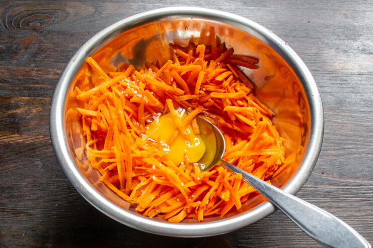 Adding an Egg to Bind the Carrot Crust A chicken egg being cracked into a bowl of grated carrots.