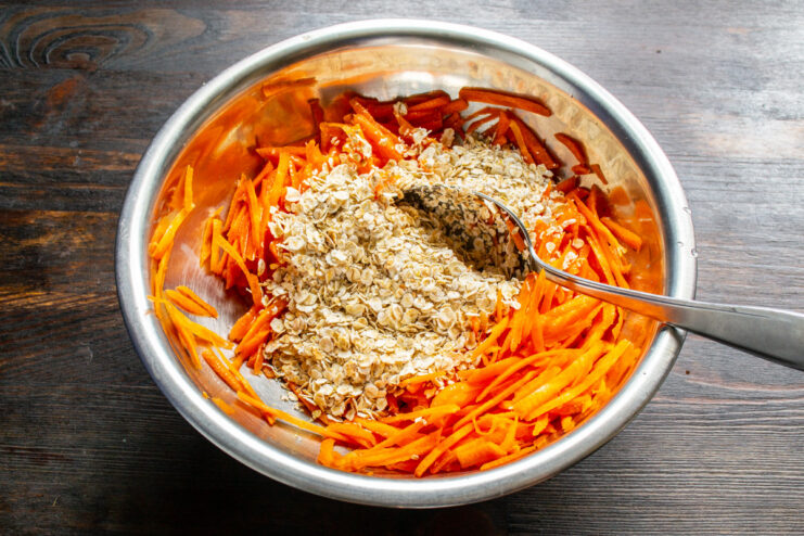 Adding Oats to the Carrot Mixture Adding quick-cooking rolled oats to the bowl with grated carrots and egg.