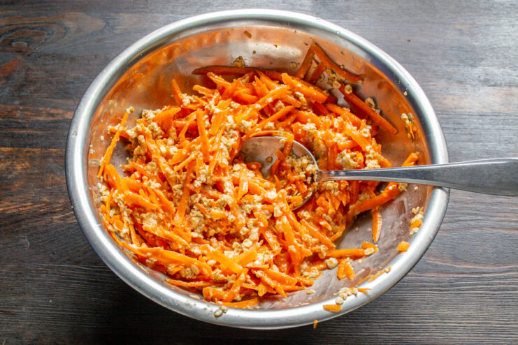 Mixing the Ingredients for the Carrot Pizza Base A spoon mixing grated carrots, egg, and oats in a glass bowl to form the pizza base.