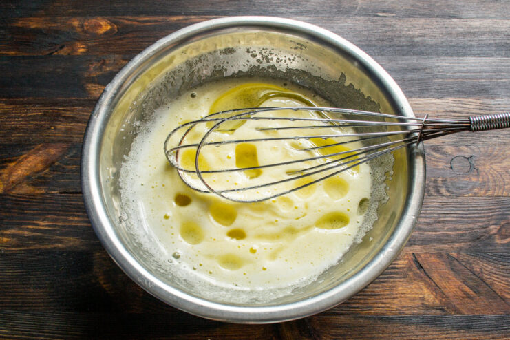 Whisking Egg and Sugar Until Smooth for Muffin Batter A hand holding a whisk, mixing an egg and sugar in a glass bowl until the mixture is pale and smooth.