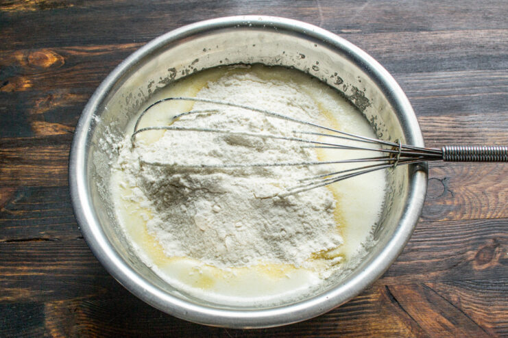Combining Wet and Dry Ingredients for Muffins Adding a scoop of flour into a glass bowl with whisked wet ingredients for the muffin batter.
