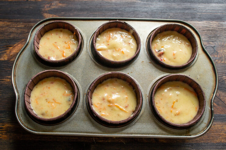 Filling the Muffin Liners with Carrot and Fig Batter A muffin tin with paper liners being filled with carrot and fig muffin batter before baking.