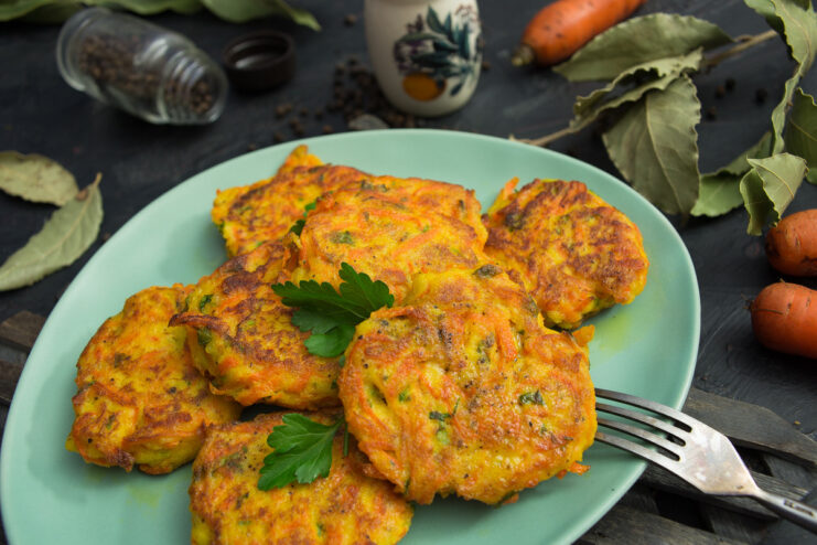 A plate of golden-brown carrot and semolina patties, garnished with fresh herbs.