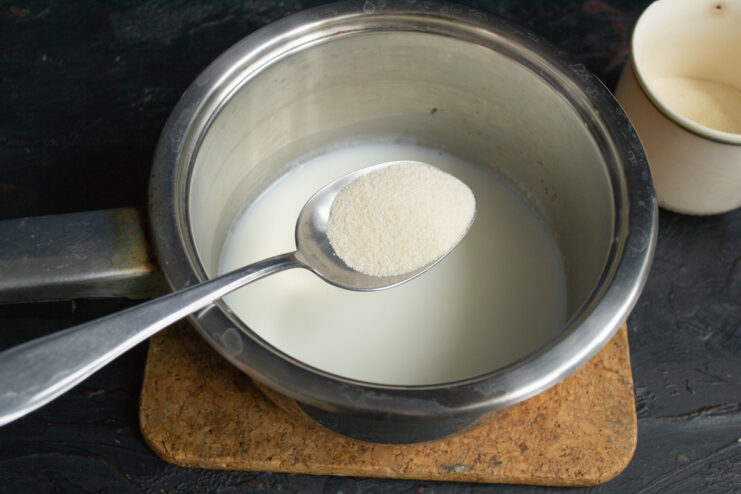Cooking semolina porridge: Pouring semolina into hot milk. A hand pouring semolina from a measuring cup into a saucepan with boiling milk.