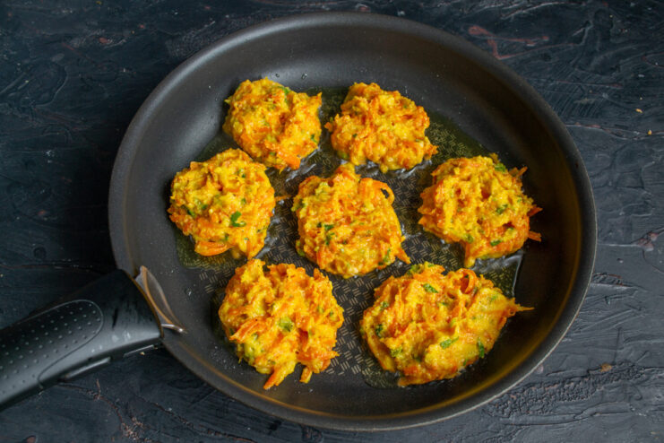 Forming carrot patties with a spoon due to the sticky texture. A spoon scooping the thick, sticky carrot patty mixture from a bowl.