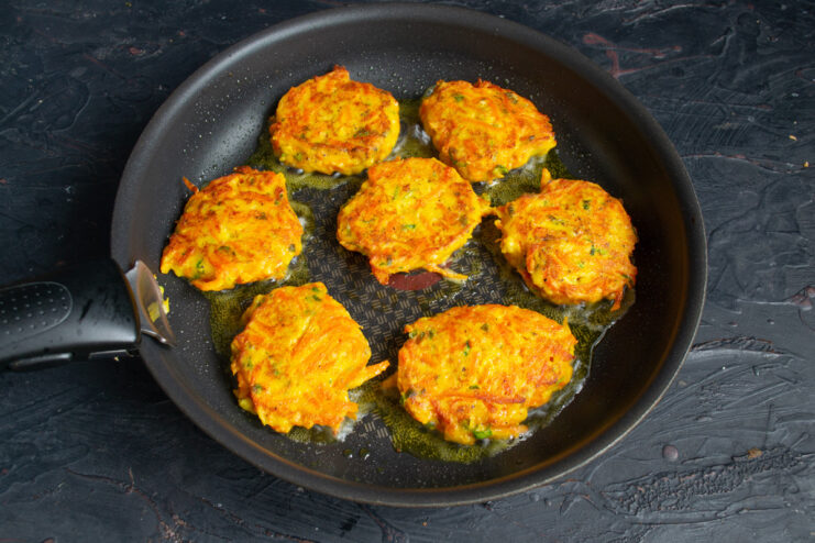 Frying the carrot patties until golden brown in a pan. Carrot and semolina patties frying in a pan, turning golden brown.
