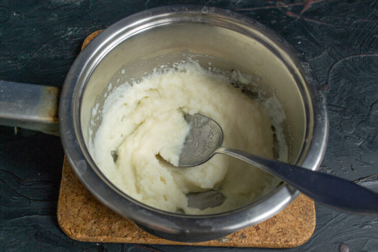 Cooling down the freshly cooked semolina porridge. A saucepan with thick, cooked semolina porridge cooling on a countertop.