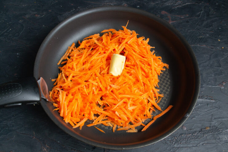 Preparing carrots for the patties by grating them. A hand grating fresh carrots on a coarse box grater.