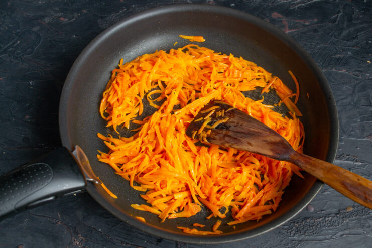 Sautéing grated carrots in a pan until tender. Grated carrots being sautéed in a frying pan with a spatula.