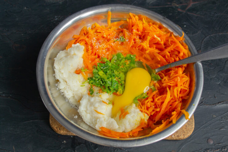 Adding an egg to bind the carrot patty mixture. A large chicken egg being cracked into the bowl with the carrot and semolina mixture.
