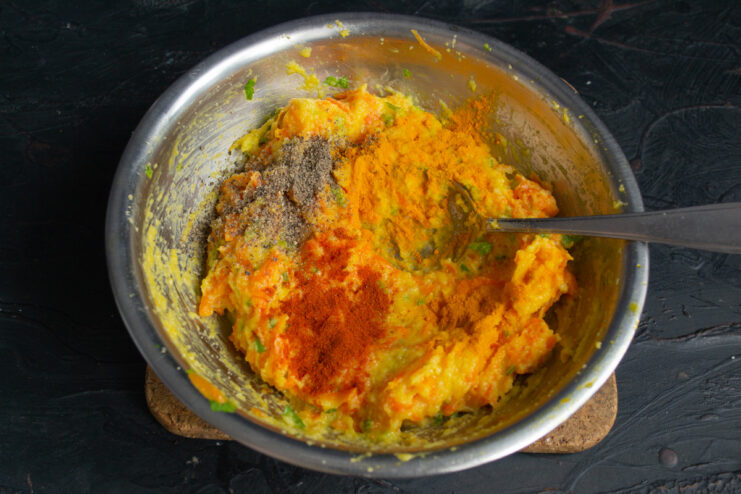 Seasoning the mixture with paprika, turmeric, and black pepper. Spices like paprika and turmeric being added to the carrot patty mixture in a bowl.
