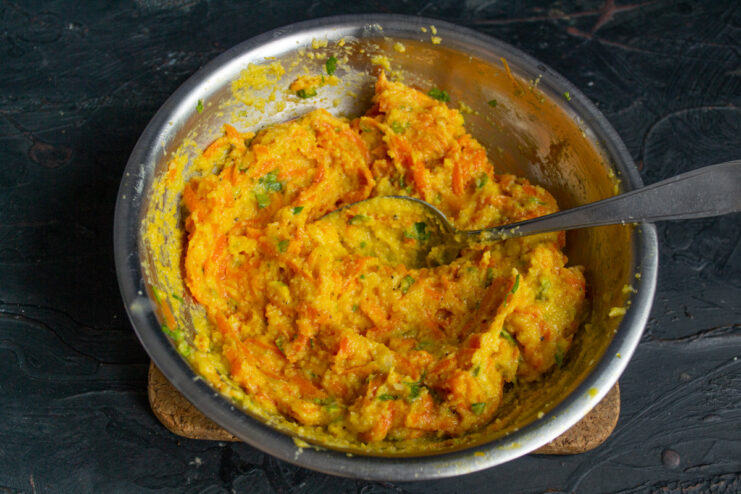 Thoroughly mixing all the ingredients for the carrot patties. A spoon mixing the carrot, semolina, egg, and spice mixture in a bowl.