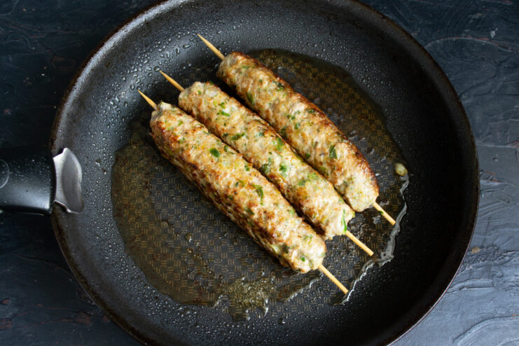 Frying the kebabs until they are perfectly golden brown on all sides. Kebabs sizzling in a pan, being turned to cook evenly.