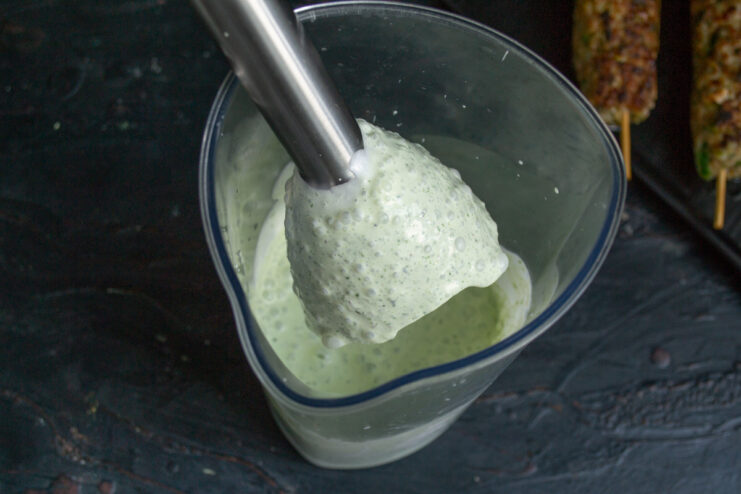 Preparing a cool and refreshing yogurt sauce with mint and cilantro. A blender jar with yogurt and fresh herbs for making the dipping sauce.