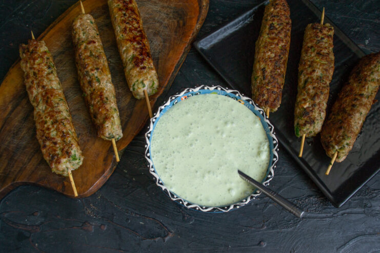 Final presentation of Egyptian kebabs with yogurt sauce and bread. A serving plate with Egyptian meat kebabs, a bowl of yogurt sauce, and fresh bread.