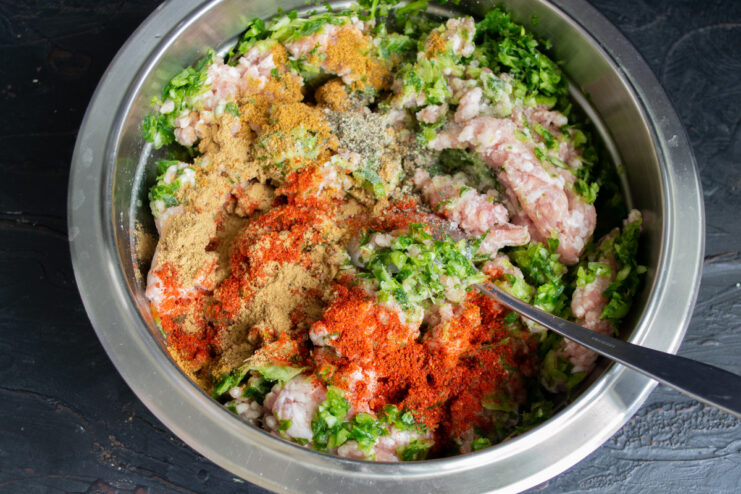 Adding spices like paprika and curry to the ground meat for the kebabs. Spices being added to the ground meat mixture in a bowl.