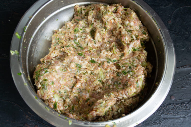Kneading the ground meat mixture by hand to combine all ingredients. Hands mixing the seasoned ground meat in a bowl for the kebabs.