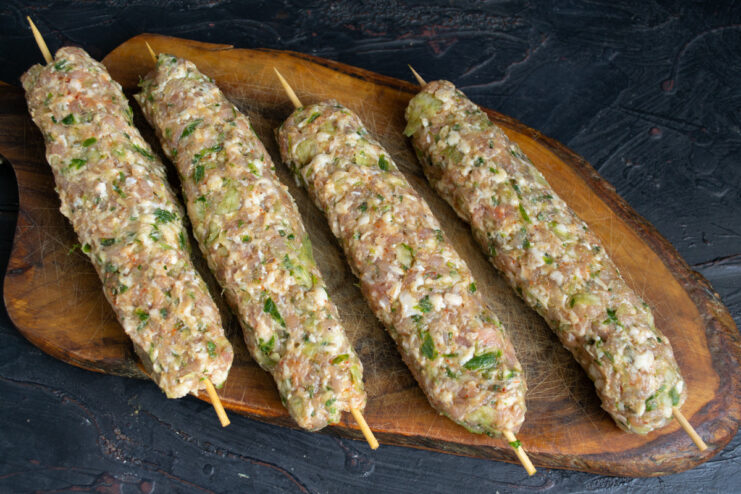 How to form the Egyptian-style kebabs around the wooden skewers. A hand shaping the ground meat mixture around a wooden skewer to form a kebab.