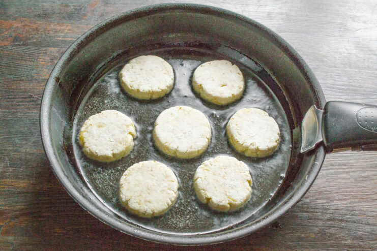 Frying the Syrniki - Flattening the balls into patties in the pan. Syrniki being flattened with a spatula in a hot frying pan with oil.