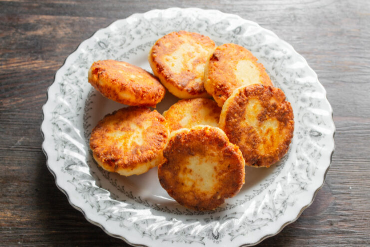 Serving Savory Syrniki - Best enjoyed warm with a dollop of smetana. A plate of ready-to-eat savory syrniki with cheese, served with a side of smetana.